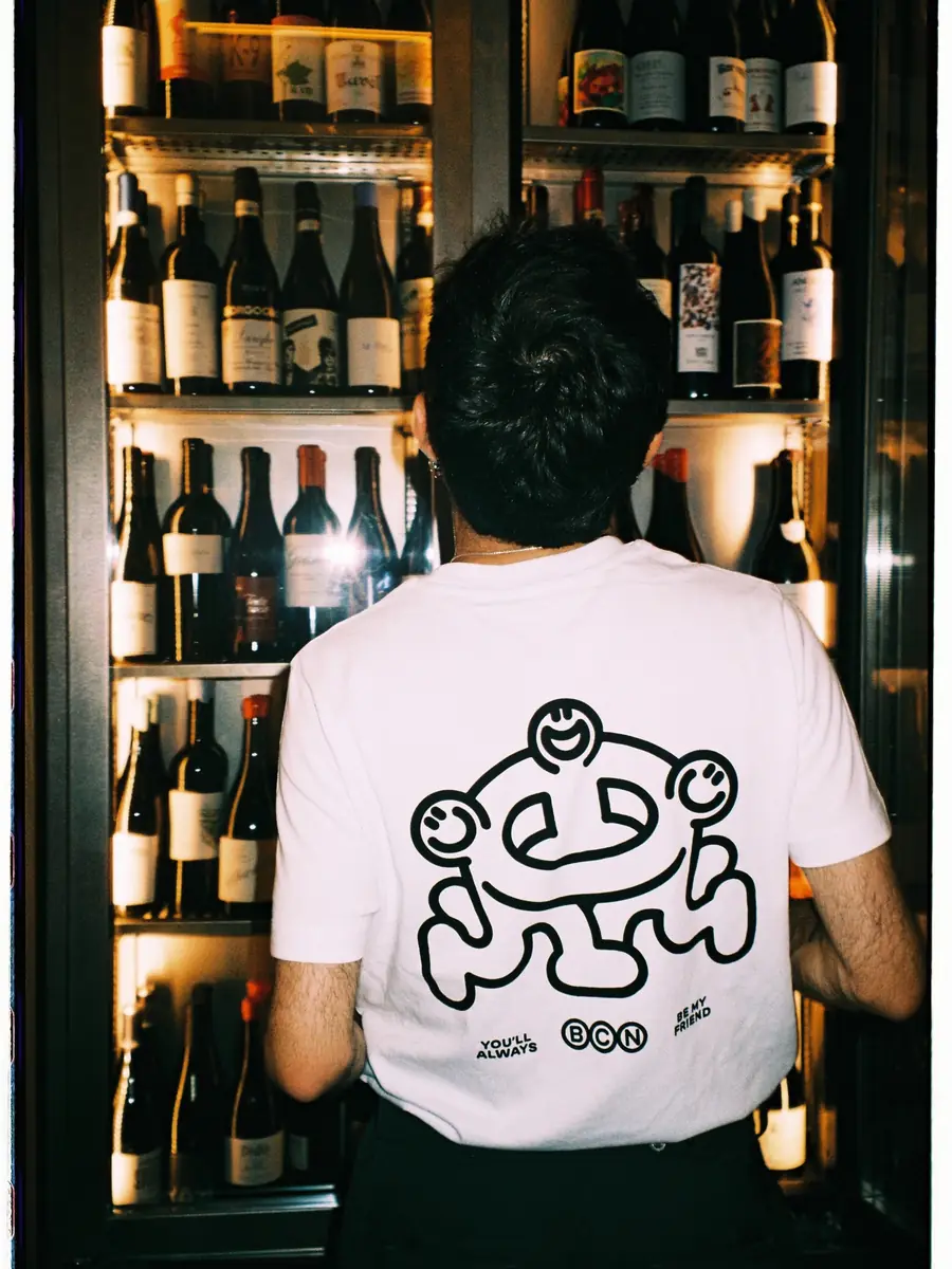 A waiter seen from behind, with the Amicks mascot on his T-shirt, in front of the wine fridge