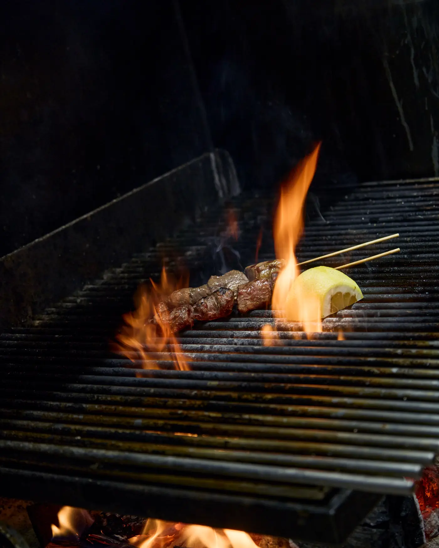 Meat skewer with lemon cooking over the flames of the grill