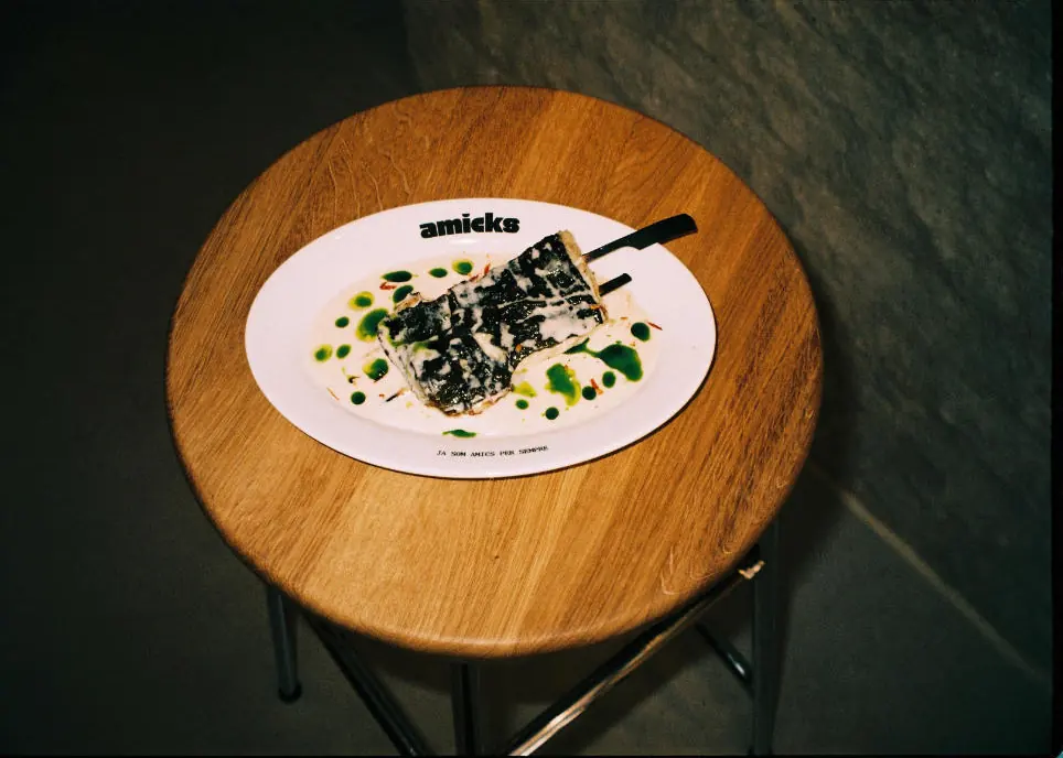 A small plate with the Amicks logo on a wooden stool