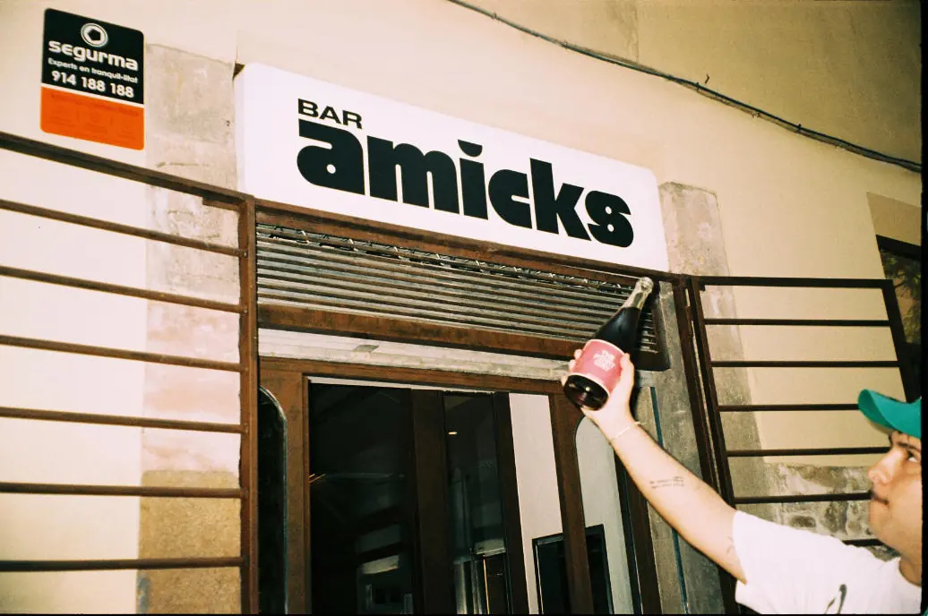 A waiter hangs a bottle next to the Bar Amicks sign