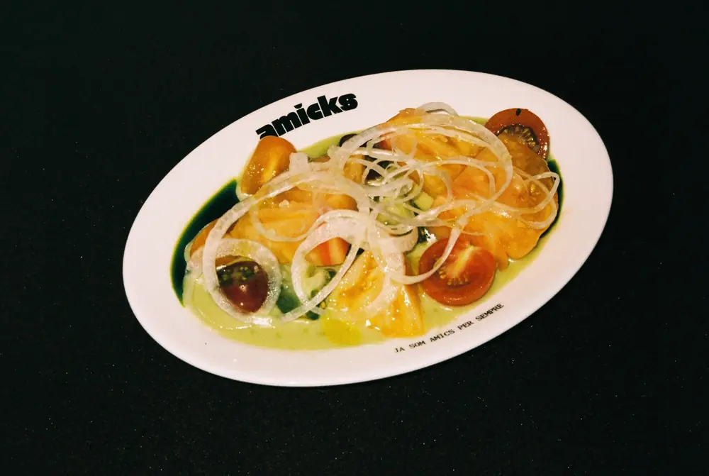 Seasonal tomato salad with onion, on a plate with the Amicks logo