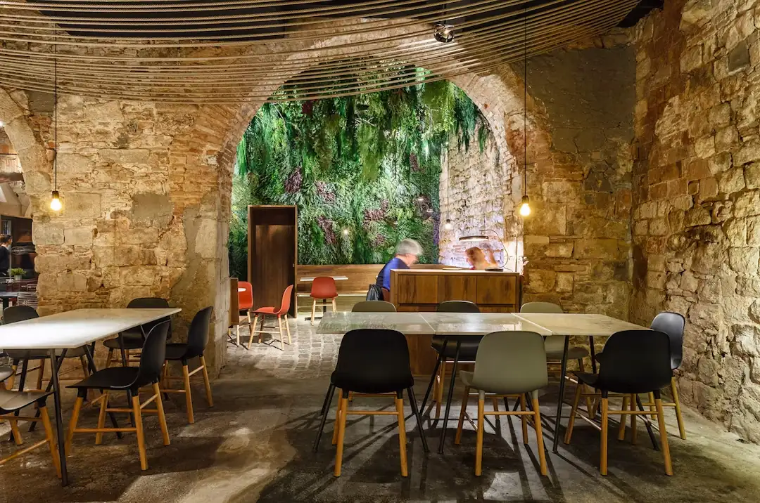 La mesa larga del comedor, bajo el arco y la pared de vegetación