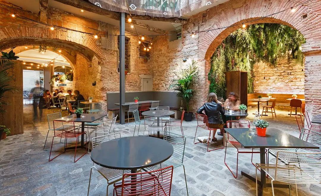 La terraza interior de La Bona Sort, con mesas y plantas bajo los arcos de piedra