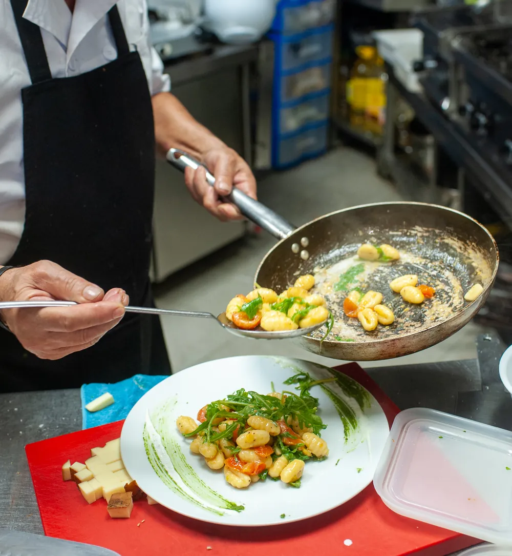 Un cocinero saltea en la sartén y emplata en la cocina de Via Napoli