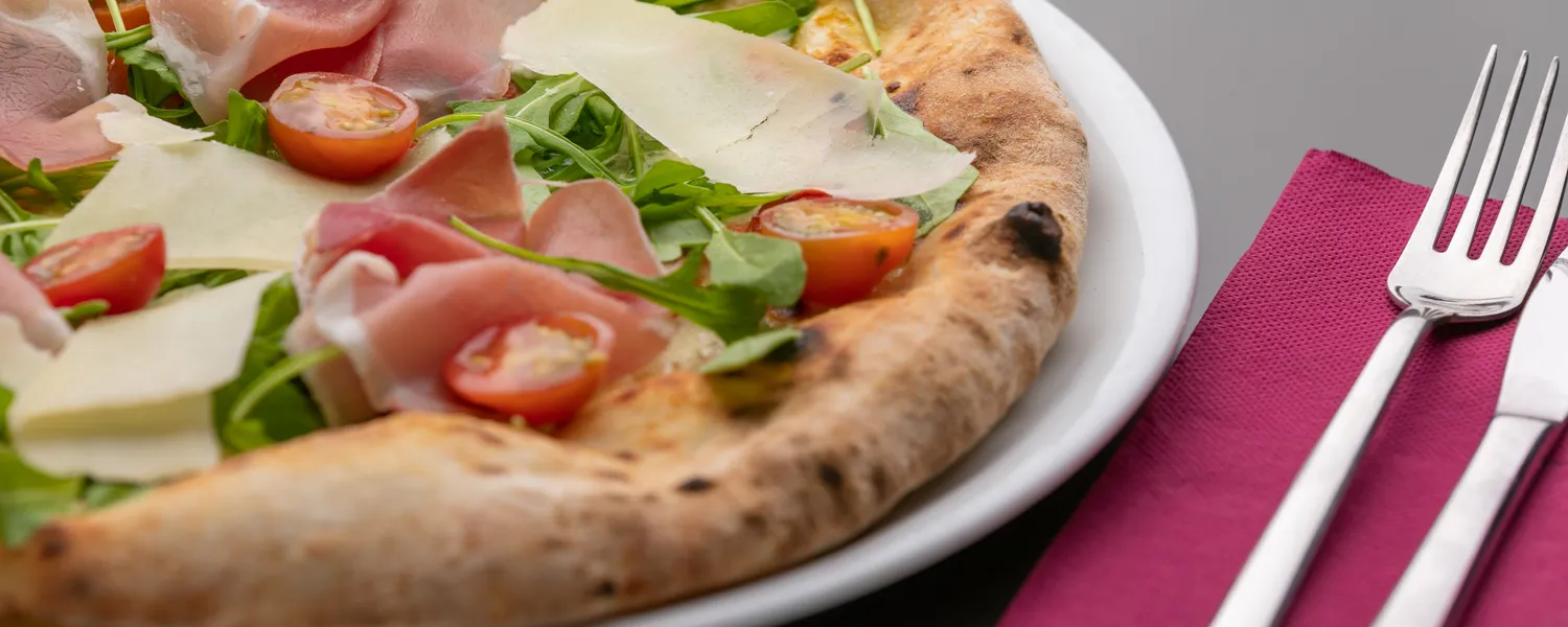 Pizza con jamón, lascas de parmesano, rúcula y tomates cherry