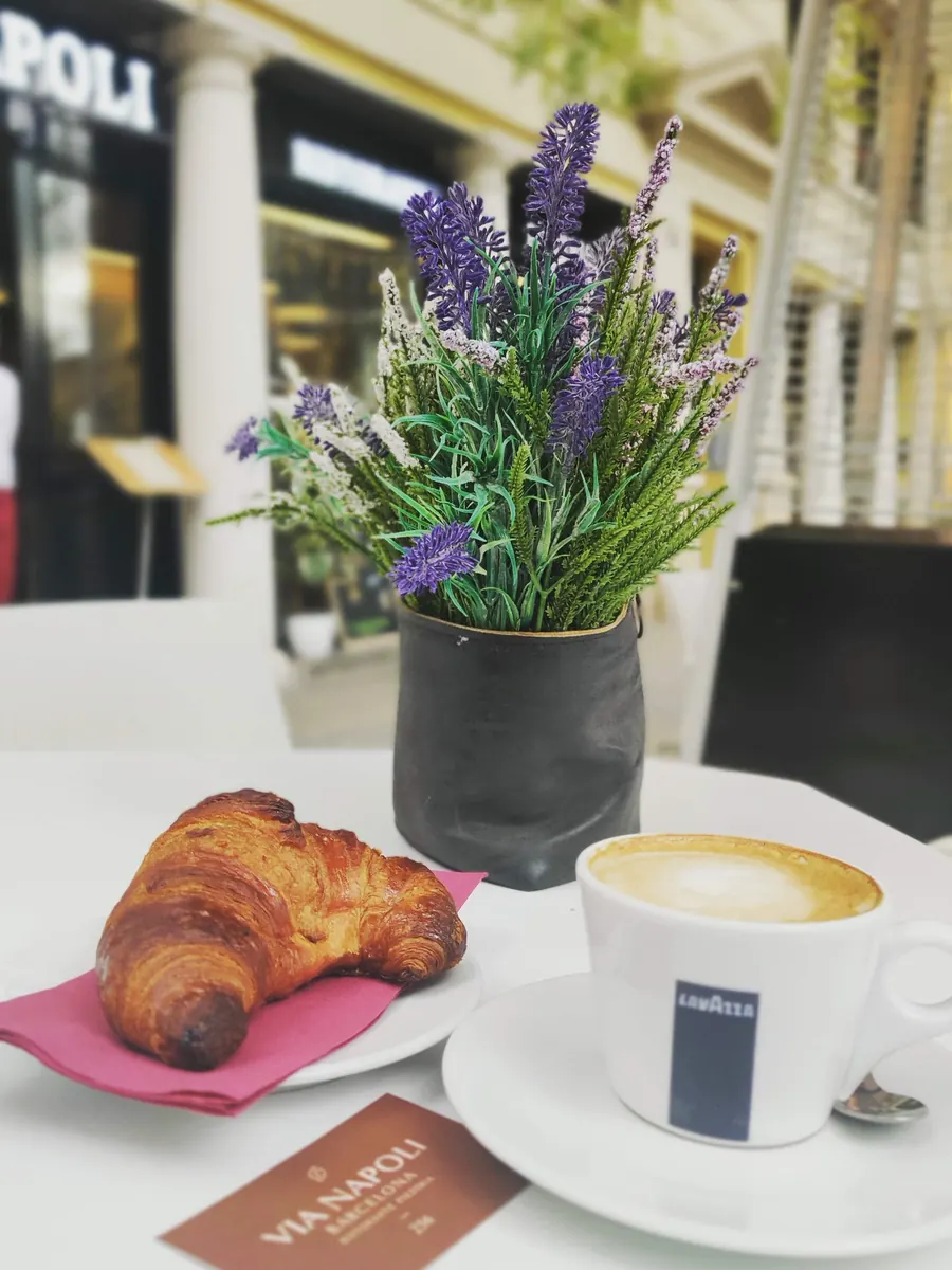 Un cruasán y un capuchino en una mesa de la terraza, junto a un tiesto de lavanda
